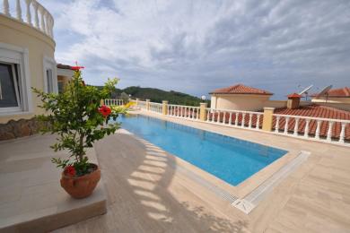 Außenansicht einer Villa in Alanya mit einem privaten Pool mit blauen Fliesen und einer hellen, sonnigen, luxuriösen Atmosphäre.