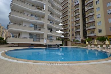 Φωτεινό, ενιαίο σαλόνι και κουζίνα σε ακίνητο στην Αλάνια με λευκά ντουλάπια, πλακάκια και άνετα καθίσματα.