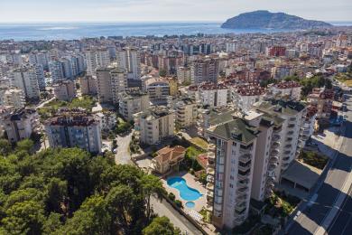 Alanyan asunnon parveke, jossa on rottinkituolit, lasipöytä ja panoraamanäkymät kaupunkiin ja merelle.