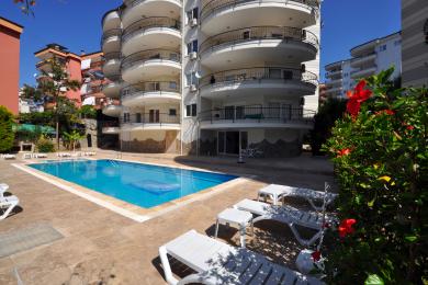 Alanya eiendom balkong med solsenger, utendørs peis og kurvmøbler, som tilbyr en avslappende, solfylt atmosfære.
