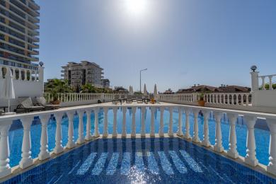 Alanya ejendomsvisning med en tennisbane med udsigt over bjerge og bygninger under en blå himmel.