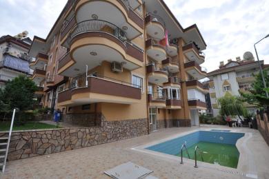 Alanya stue med varme gule vægge, flisegulve og vinduer med lette gardiner, der skaber en lys og luftig atmosfære.