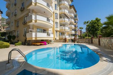 Alanya eiendom stue har mønstrete sofaer, lenestoler og varm belysning fra de gylne gardinene, som skaper en koselig atmosfære.