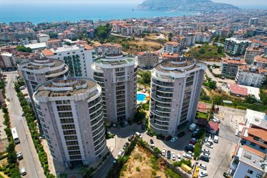 Lyst Alanya lejlighedsområde med et moderne hvidt køkken, spisebord, komfortabel sofa og flisegulv.