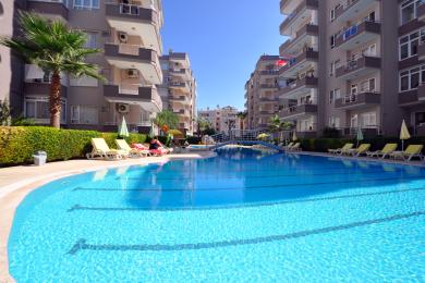 Der helle Wohnbereich des Apartments in Alanya verfügt über eine Bar mit Granitplatte, Fliesenböden und Zugang zum Balkon mit Meerblick.