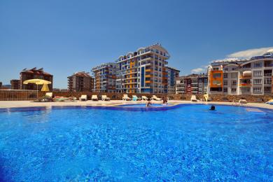 Alanya Küche mit weißen Schränken, Edelstahlkühlschrank, Fliesenboden und heller, luftiger Atmosphäre.