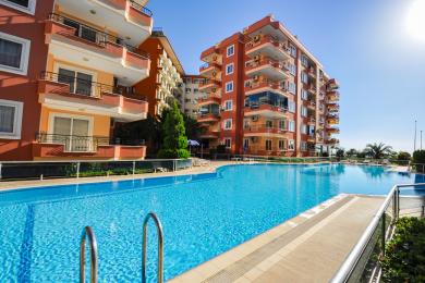 Helles Alanya Apartment Wohnzimmer mit dunklem Sofa, Fliesenböden, Essbereich und Zugang zum Balkon.