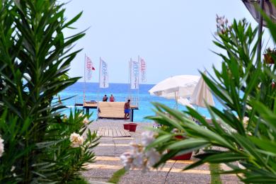 Bright Alanya balcony with wicker furniture, glass table, and sliding doors overlooking modern buildings.