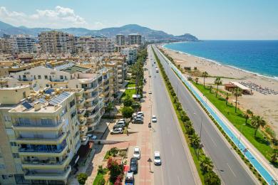 Alanya Immobilien Balkon mit Blick auf das Mittelmeer, Palmen und die Küstenstraße an einem sonnigen Tag.