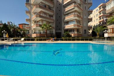 Alanya eiendomsvisning som viser en anlagt gårdsplass med steinganger og leilighetsbalkonger.