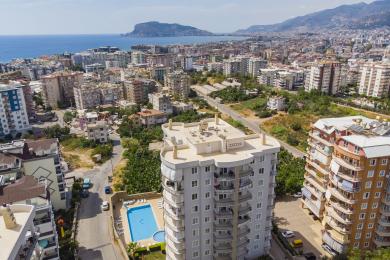 Alanya ejendom: Lyst, åbent køkken og opholdsområde med lyse træskabe og en komfortabel lædersofa.