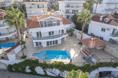 Alanya villa exterior featuring a bright blue swimming pool, palm trees, and sunny, luxurious atmosphere.