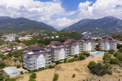 Prosluněná zimní zahrada v Alanyi s dlážděnou podlahou a velkými okny s výhledem na bazén a bujnou krajinu.