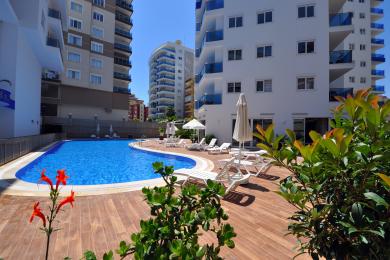 Svijetla kuhinja apartmana u Alanji s modernim bijelim ormarićima, tamnim radnim površinama, mramornim podovima i obiljem prirodnog svjetla.
