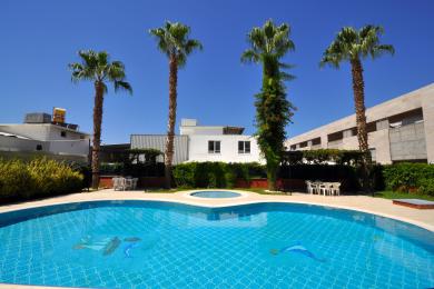 Quyoshli Alanya balkonida kafel qoplamasi, to'q sariq devorlar va tiniq moviy osmon ostida shahar manzarasi.