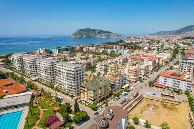Alanya kinnisvara elutuba plaatpõrandate, kollaste seinte, mugava mööbli ja ereda loomuliku valgusega, mis loob hubase atmosfääri.