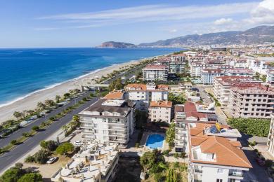 Björt, lokuð Alanya svalir með wicker stólum, borði og víðáttumiklu sjávarútsýni í gegnum gólfsíða glugga.