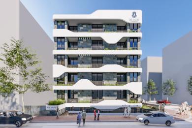 Világos alanyai apartman nappali fehér kanapéval, kék kiegészítőkkel és nyitott konyhával, márvány hátfallal.