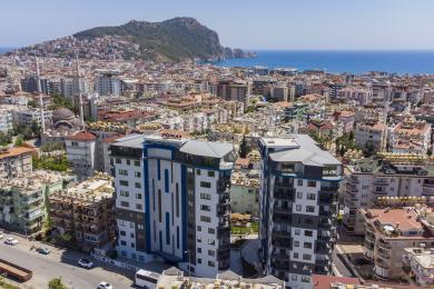 Alanya ejendom altan med glasrækværk der tilbyder lyse by- og havudsigter gennem store glasskydedøre.
