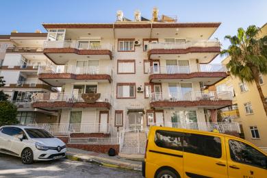 Alanya onroerend goed woonkamer met zachte roze banken, marmeren vloeren en heldere, natuurlijke verlichting die een comfortabele sfeer creëert.