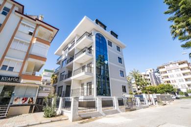 Bucătărie luminoasă într-un apartament din Alanya, cu dulapuri albe, protecție de fundal neagră, podele de marmură și ferestre mari.