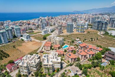 Balkon nekretnine u Alanji sa nameštajem od pruća, staklenim stolom i pogledom na grad pod jarkim, prirodnim svetlom.