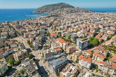 Alanya eiendom balkong med kurvmøbler, flisebord, glassrekkverk og lys, solrik utsikt over byen.