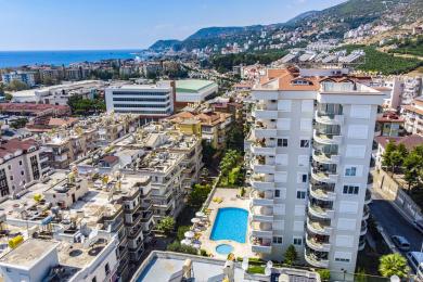 Keng Alanya balkonida kafel qoplamasi, shisha panjaralar va shahar va dengizning panoramik manzaralari quyosh nurida yuvilgan.