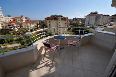 Alanya-Immobilienbalkon mit Fliesenboden, Metallgeländer, Sitzgelegenheiten und einem hellen, sonnigen Stadtbildblick.