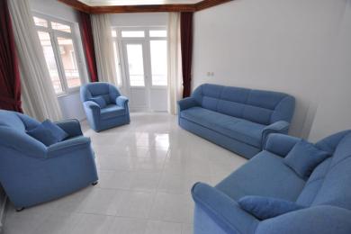 Alanya eiendom stue med blå sofaer, flislagte gulv, sterkt naturlig lys og tilgang til balkong.