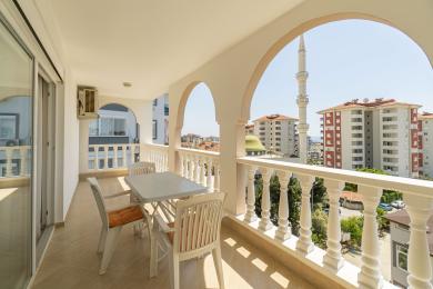 Balkon nekretnine u Alanji sa belim lukovima, balustradom, trpezarijskim nameštajem na otvorenom i pogledom na grad uključujući džamiju.