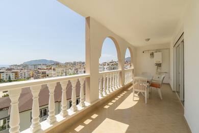Alanya balkon met boogvormige openingen, witte balustrade, tegelvloer en uitzicht op de stad, waardoor een heldere, luchtige sfeer ontstaat.