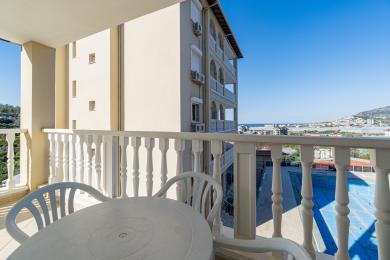 Balkon w Alanyi z białymi balustradami, plastikowymi meblami i jasnymi, słonecznymi widokami na miasto.