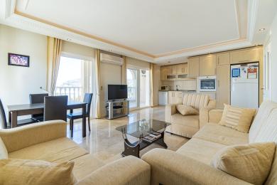 Svijetli apartman u Alanji, dnevni boravak s mramornim podovima, bež sofama, blagovaonicom i integriranom kuhinjom.