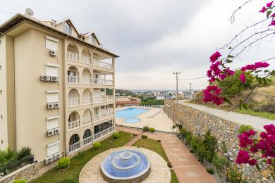 Alanya property view featuring a pool, fountain, and balconies with a city and sea view in the background.