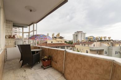 Alanya ejendom balkon med marmorgulv, kurvemøbler og udsigt over byen under en skyet himmel.