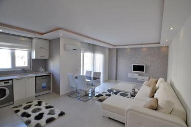 The living area of this Alanya apartment features a modern kitchen, a dining set, a textured wall, and a comfortable white sofa.