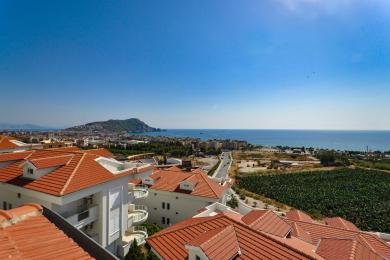 Pogled na nekretninu u Alanji prikazuje crvene krovove, bijele zgrade i zadivljujuću panoramu Sredozemnog mora pod vedrim plavim nebom.