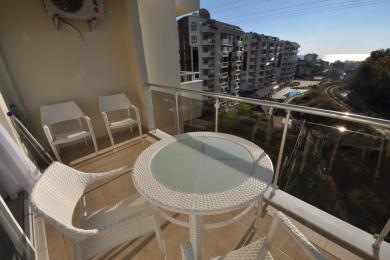 Alanya-Immobilienbalkon mit weißen Korbmöbeln, Glastisch und heller, sonniger Atmosphäre mit Blick auf die Landschaft.