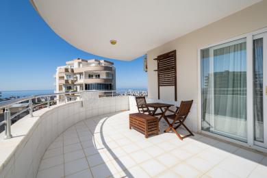Balcon al proprietății din Alanya cu pardoseală din gresie, mobilier din lemn și atmosferă luminoasă și însorită, cu vedere la oraș și la mare.