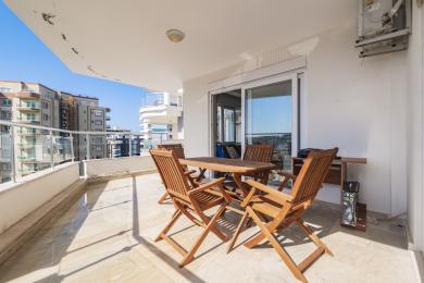 Proprietate în Alanya cu balcon cu masă și scaune din lemn, podea de marmură, lumină puternică a soarelui și vedere la oraș.