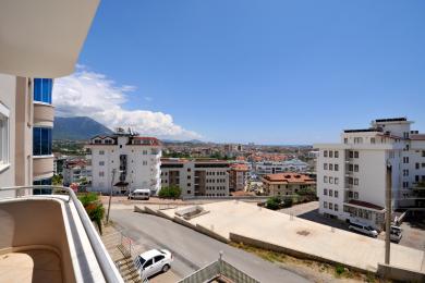 Alanya eiendom balkongutsikt som viser bybygninger, fjell og en lys og solrik atmosfære.