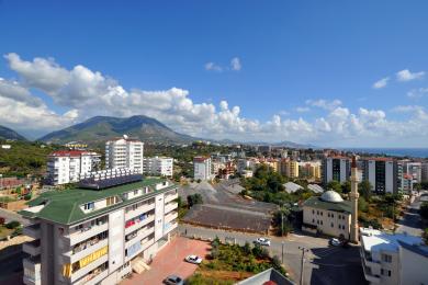 Utsikt over Alanya som viser byen, fjellene og havet under en lys, skyet himmel.