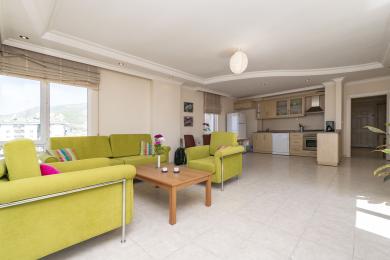 Helles Alanya Apartment Wohnzimmer mit offener Küche, Fliesenböden und bequemen, modernen grünen Sitzgelegenheiten.