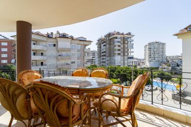 Balcon al proprietății din Alanya cu mobilier din ratan, masă de sticlă și vedere luminoasă și însorită asupra peisajului urban.