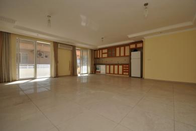 Lichte, open Alanya woonkamer met tegelvloeren, toegang tot het balkon en een moderne keuken met houten kasten.
