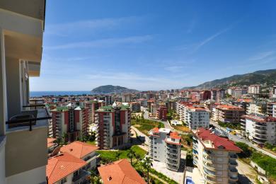 Alanya ejendom balkonudsigt, der viser bybillede, Middelhavet og en lys, solrig atmosfære.