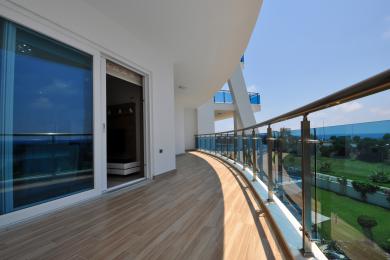 Balkon nekretnine u Alanji sa podom od pločica koje izgledaju kao drvo, staklenom ogradom i svetlom, sunčanom atmosferom.