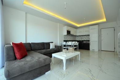 Obývací pokoj apartmánu v Alanyi se pyšní moderní kuchyní, mramorovými podlahami a teplým, zapuštěným osvětlením, které vytváří světlý a příjemný prostor.