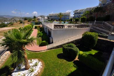 Alanya property featuring lush landscaping, a red brick walkway, and a sunny rooftop terrace with outdoor seating.